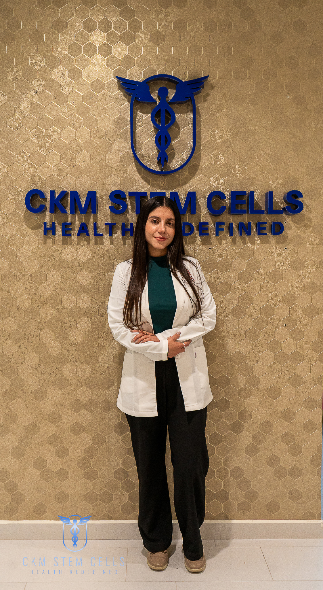 Young professional wearing a navy suit and glasses, standing with hands in pockets in a modern office lobby next to a gray sofa and potted plant.